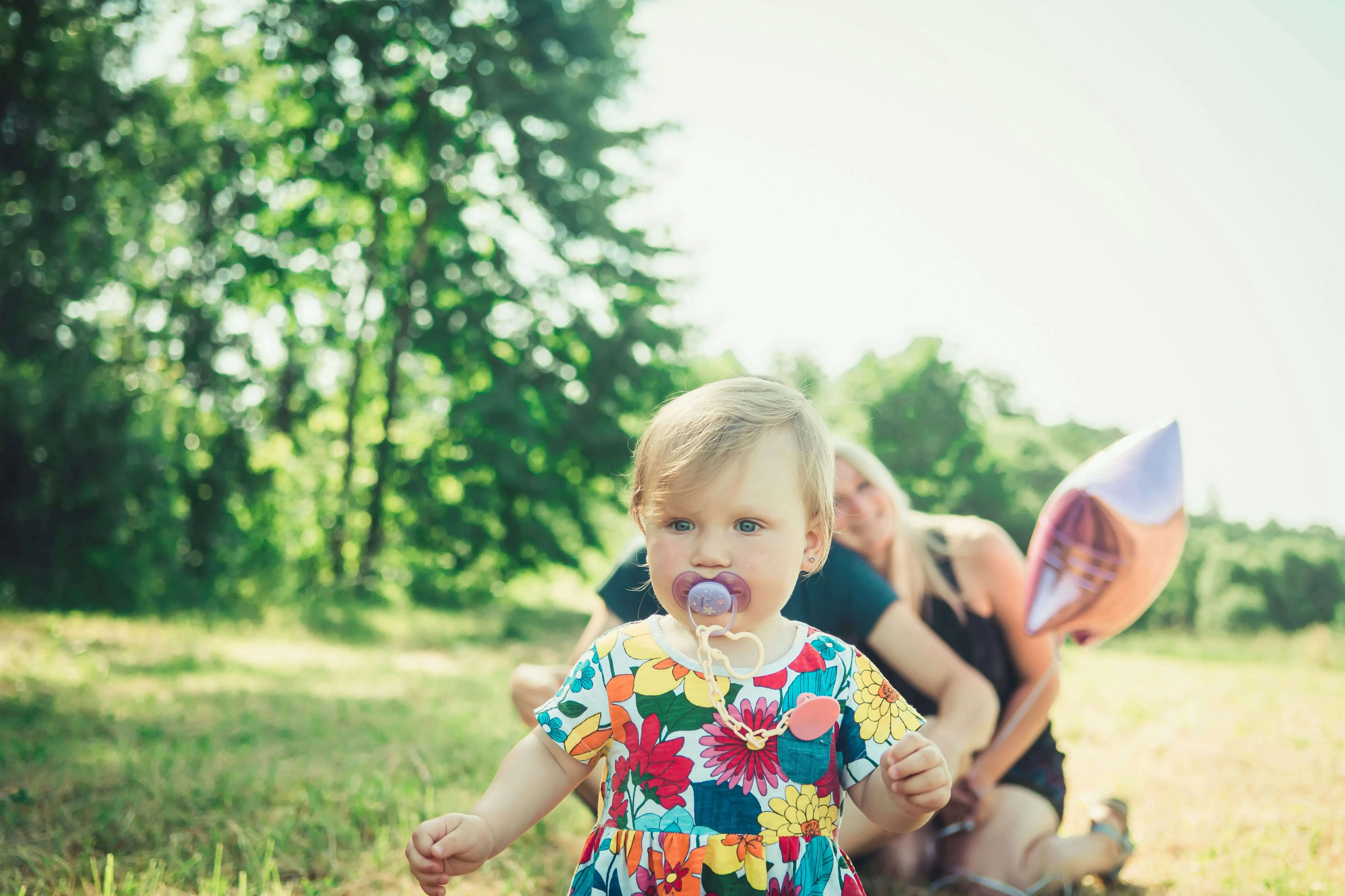 Baby with pacifier outdoors near family and balloon