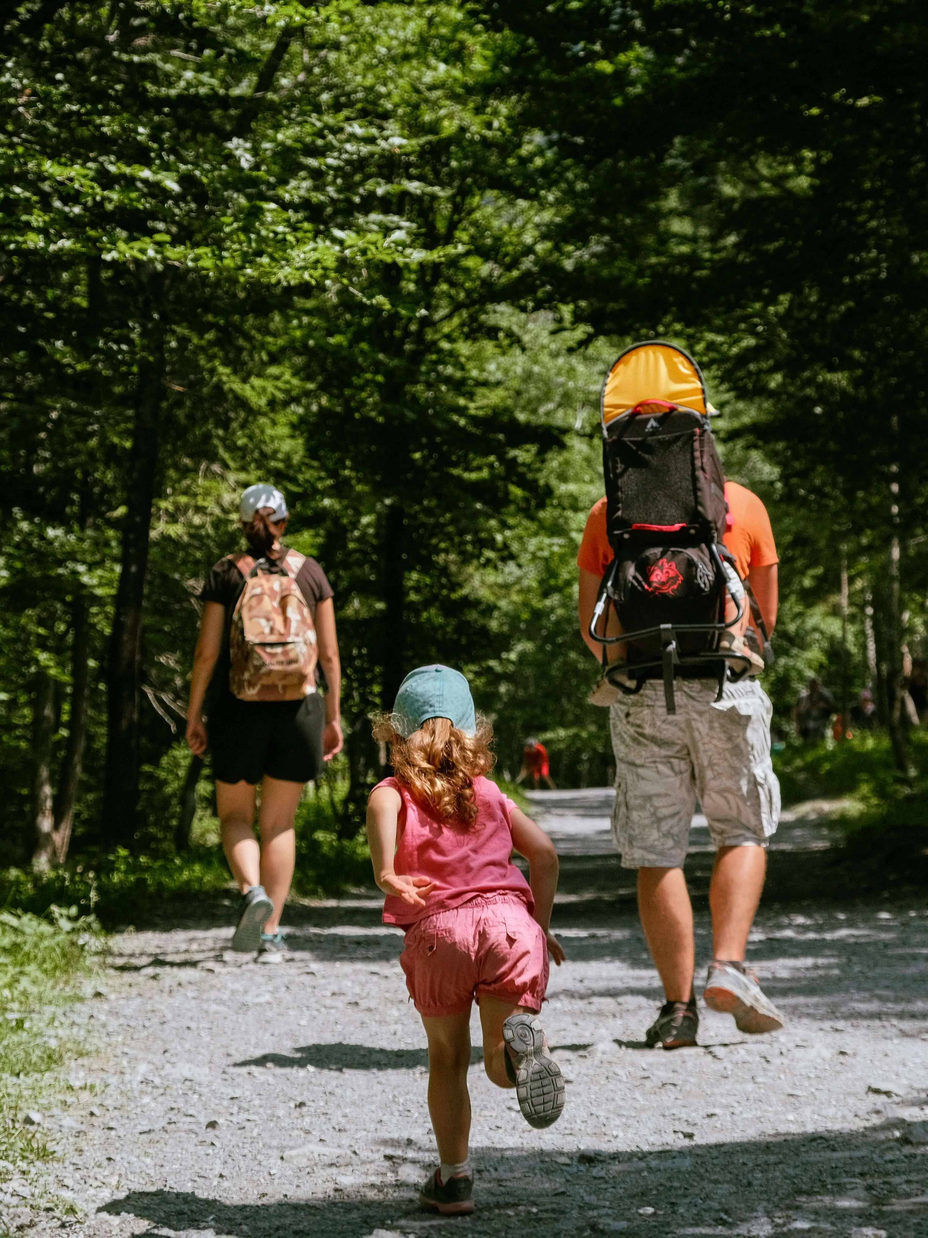 Family hiking on forest trail, child running ahead.
