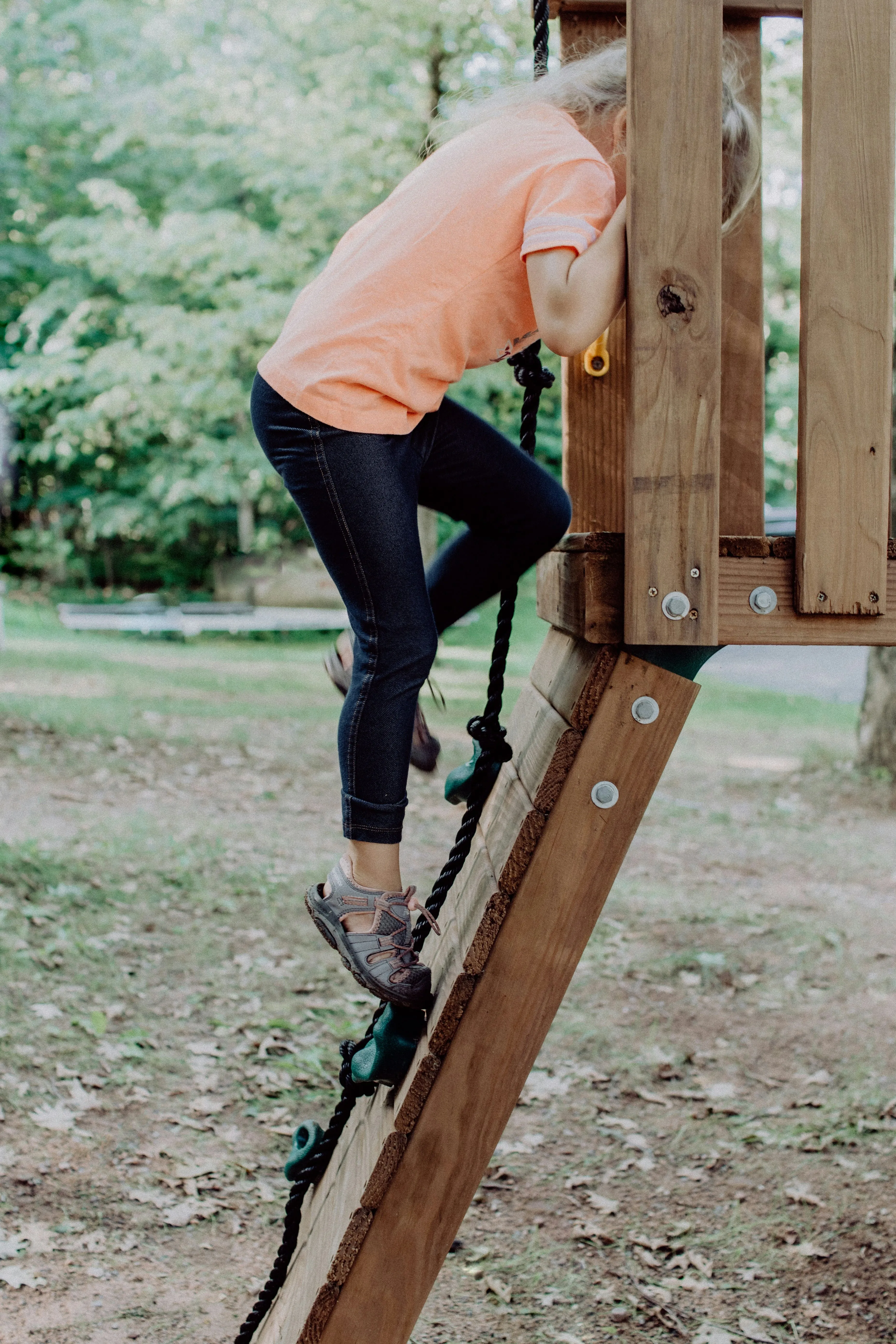 Child climbing wooden playground ladder outdoors.