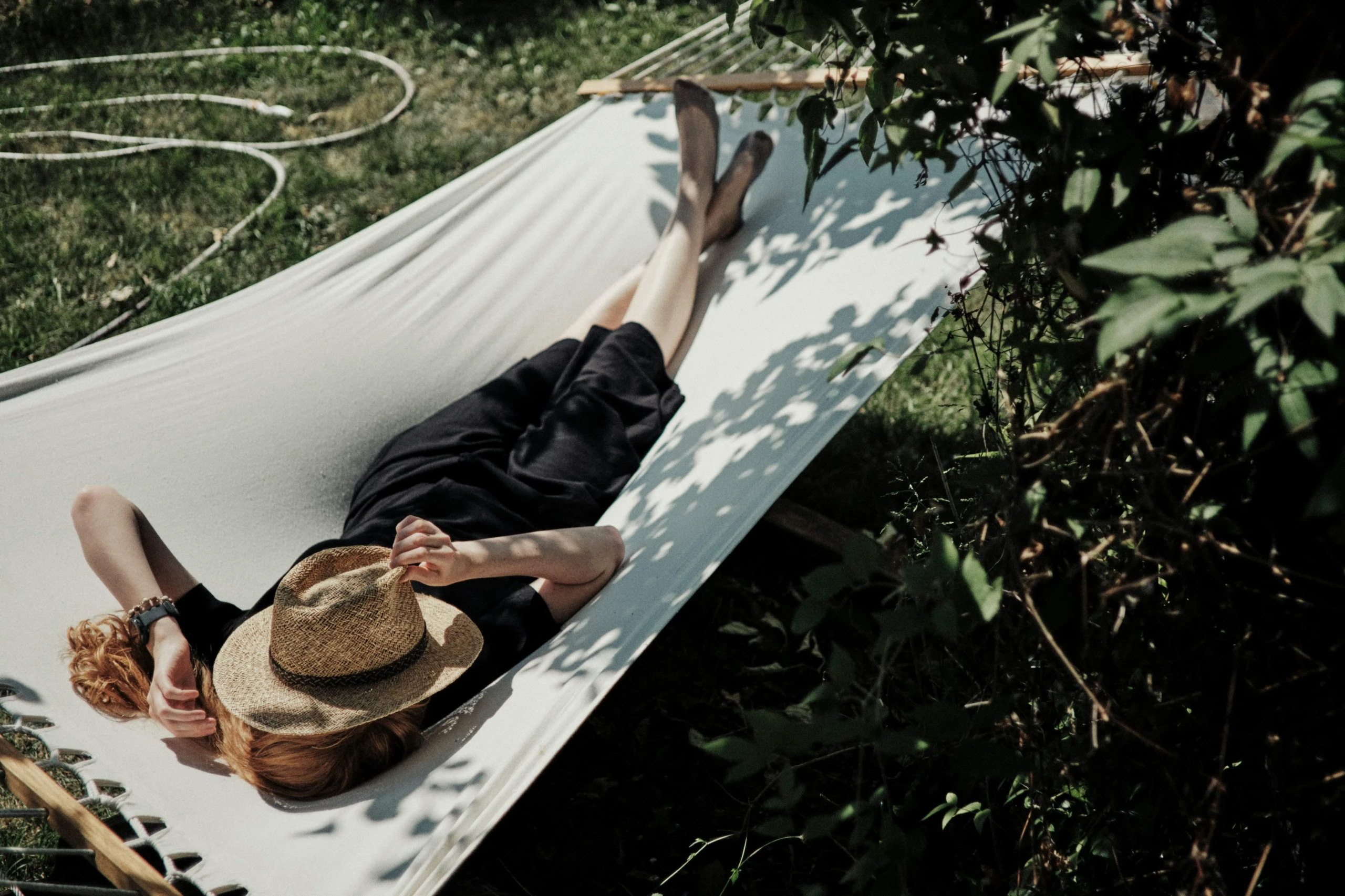 Person relaxing on hammock in sunny garden.
