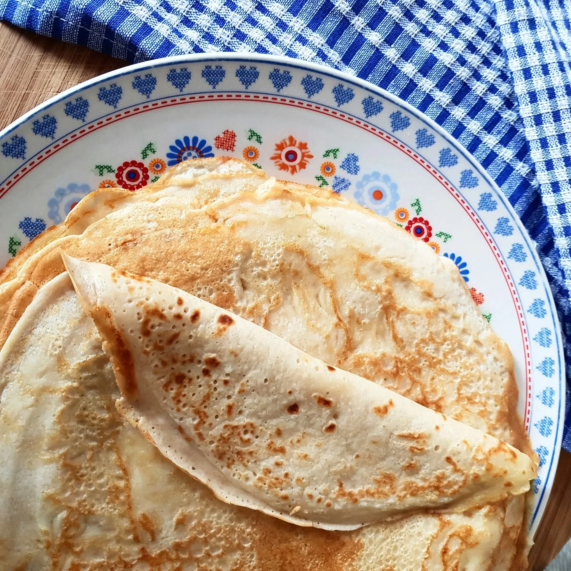 Homemade crepes on decorated plate with checkered cloth.