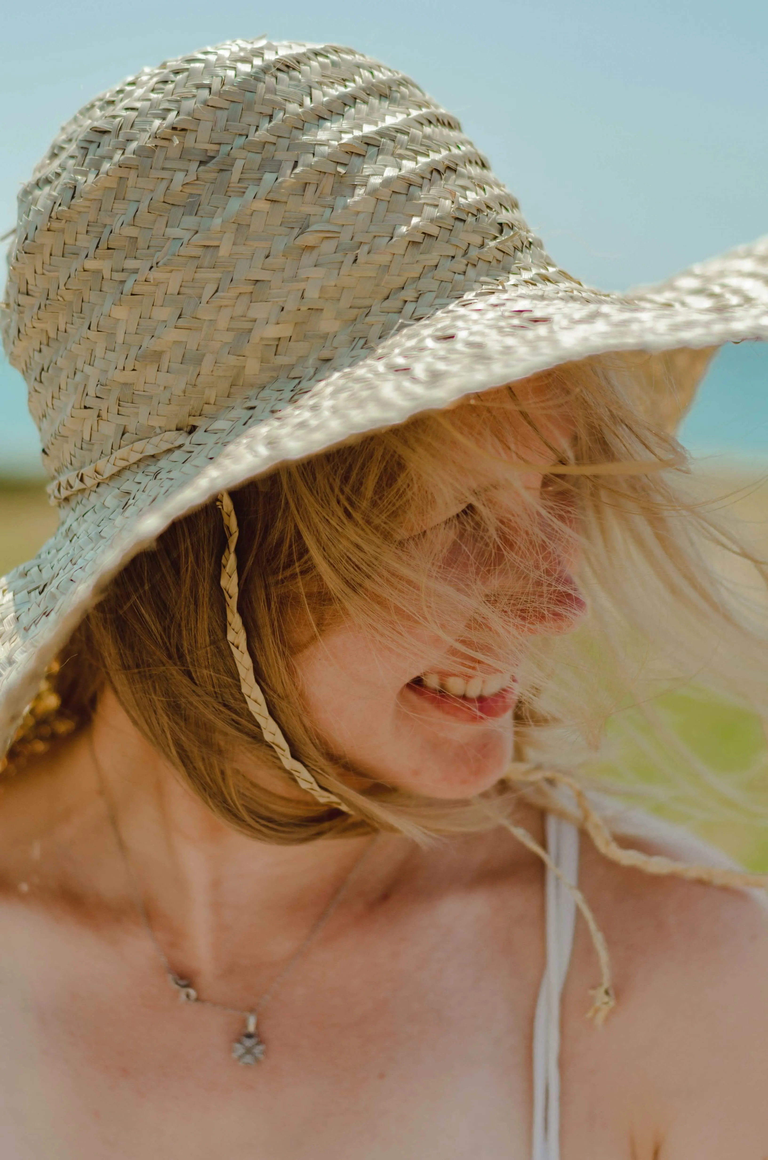 Woman in sunhat smiling on a windy beach