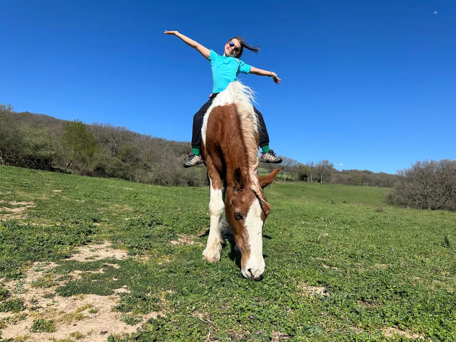 Person joyfully riding a horse in a green field.